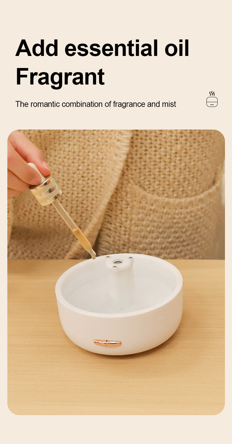 White diffuser on a wooden surface with a hand adding essential oil using a dropper.