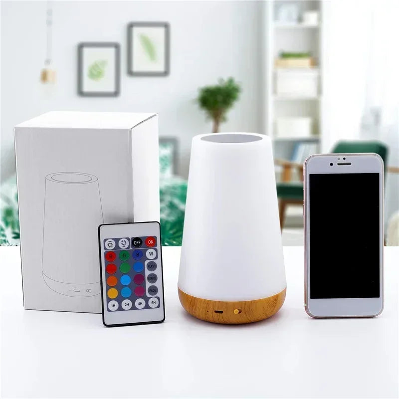 White diffuser with wooden base, remote control, and smartphone on a table.
